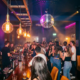 Belebte Bar mit Discokugel, Edison-Glühbirnen und tanzender Menge in Magenta- und Bernsteinlicht.