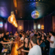 Belebte Bar mit Tanzfläche, Edison-Glühbirnen und Discokugel tauchen junge Menge in goldenes und violettes Licht.