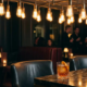 Cocktail auf dunkler Marmorbar in stimmungsvoller Lounge mit Edison-Glühbirnen und Ledersitzen im Hintergrund.