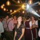 Lachende Frau im Blumenkleid auf Oktoberfest-Tanzfläche, Freunde in Tracht, Discokugel verstreut goldenes Licht.