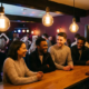 Junge Menschen lachen entspannt an einer beleuchteten Bartheke, warme Edison-Glühbirnen tauchen die lebhafte Bar in goldenes Licht.
