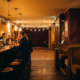 Gemütliche Münchner Bar am Abend mit leuchtendem Holztresen, Edison-Glühbirnen und Gästen auf Barhockern in warmem Goldlicht.