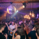 Disco-Kugel wirft prismatisches Licht auf feiernde Gäste in einer stimmungsvollen Münchner Bar mit Edison-Glühbirnen und lila-goldener Atmosphäre.