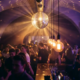 Drehende Discokugel verstreut goldenes Licht über tanzende Menschenmenge in Münchner Bar mit Edison-Glühbirnen und violettem Ambiente.