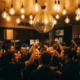 Discokugel wirft goldenes Licht auf belebte Münchner Bar mit tanzenden Gästen und Edison-Glühbirnen über der Tanzfläche.