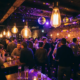 Münchner Bar mit Tanzfläche, Edison-Glühbirnen und Discokugeln tauchen die Menge in Gold- und Violetttöne.