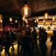 Tanzende Silhouetten in einer Münchner Bar mit warmem Ambicelicht großer Edison-Glühbirnen und goldener Atmosphäre.