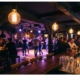 Tanzende Silhouetten in einer Münchner Bar mit warmem Bernstein- und Violettlicht, Edison-Glühbirnen und beschlagenen Gläsern auf der Theke.