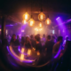 Tanzfläche eines Münchner Clubs mit warmem Bernstein- und Violettlicht, glühenden Edison-Lampen und bewegten Silhouetten in atmosphärischem Dunst.