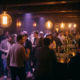 Tanzfläche eines Münchner Clubs in warmem Bernstein- und Violettlicht mit glühenden Edison-Lampen über bewegter Menge.