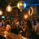 Belebte Bar mit Tanzfläche, Edison-Glühbirnen und Diskokugel, die goldenes und blaues Licht über feiernde Gäste streut.