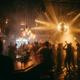 Belebte Bar mit Tanzfläche, Edison-Glühbirnen und Diskokugel tauchen tanzende Silhouetten in goldenes Licht.