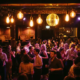 Tanzende Menschen in belebter Bar mit Edison-Glühbirnen, Discokugel und warmem Amber-Licht in stimmungsvollem Ambiente.