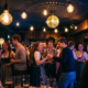 Tanzende Menge in Dirndl und Freizeitkleidung unter Edison-Glühbirnen und Diskokugel in stimmungsvoller Bar.